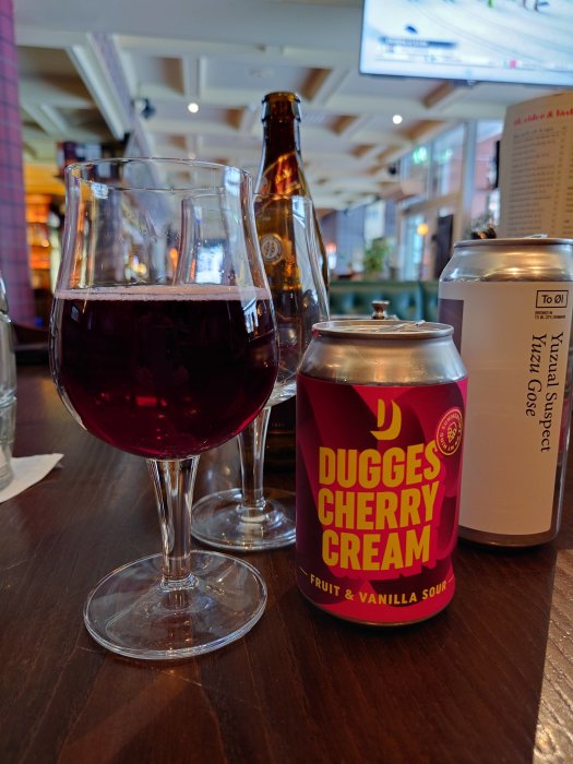 Ett glas röd öl, kanburk Dugges Cherry Cream, flaska och meny på bar.