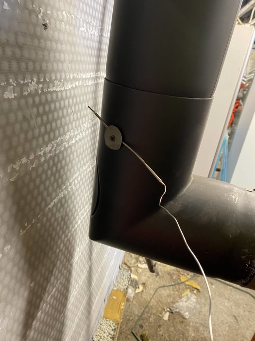 Rör med sensor fäst mot bubbelfolieisolerad vägg, kabel leder bort, byggmiljö med skräp på golvet.