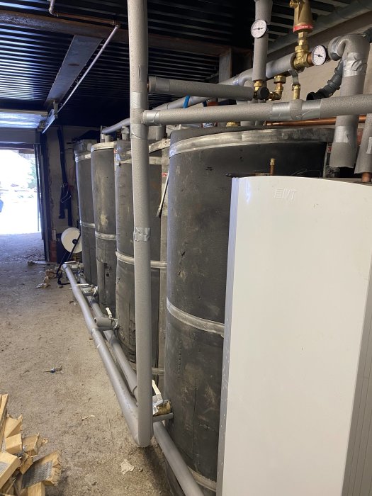 Industriella tankar och rörledningar i ett lager, möjligtvis för vätskehantering eller uppvärmningssystem.