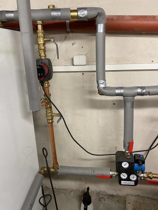 Värmeinstallation med kopparrör, ventiler, isolering och en cirkulationspump på en vägg.