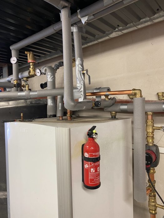 VVS-installationer, isolerade rör, fördelningsbox, brandvarnare, tryckmätare, brandsläckare på väggen.