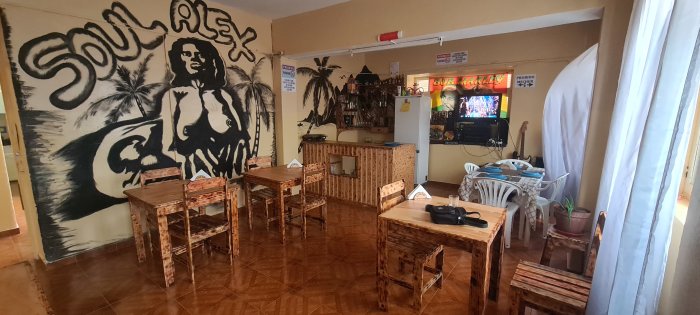 Restaurang eller café med reggae-tema, träbord, konstnärlig muralmålning, avslappnad atmosfär, TV på väggen.