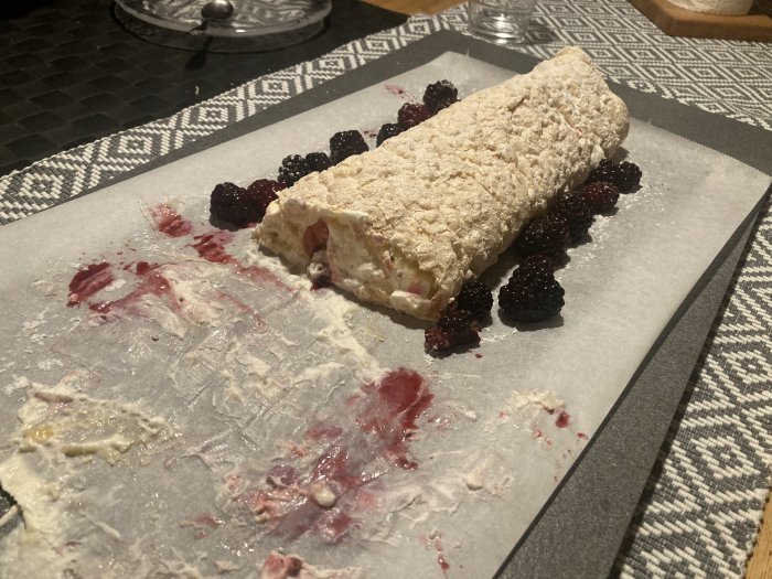 Ett uppätet bakverk, troligtvis en pavlova eller rulltårta, med bär uppdukat på bakplåtspapper och bord.