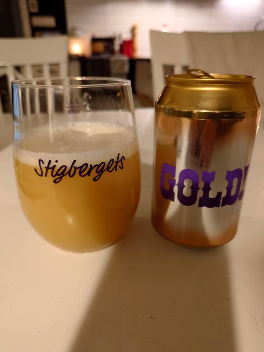 Ölglas med skum på ett bord, bredvid en guldig burk med texten "GOLD".