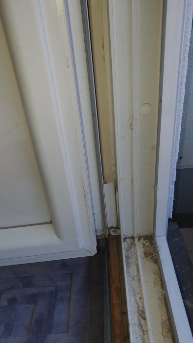 Vit, hopfällbar dörr, smutsiga spår, trätröskel, beige matta, slitage, inomhusmiljö, behov av rengöring.