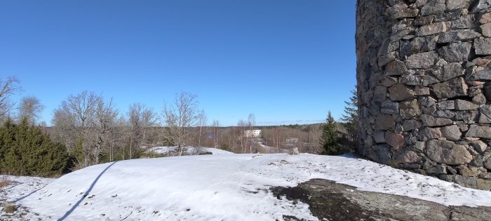 Solsken, snö, stenmur, skog, byggnader i bakgrunden, blå himmel, början på vår.