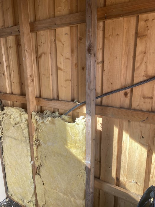 Inbyggnadsarbete med synliga träreglar och gul isolering i en väggkonstruktion under renovering.