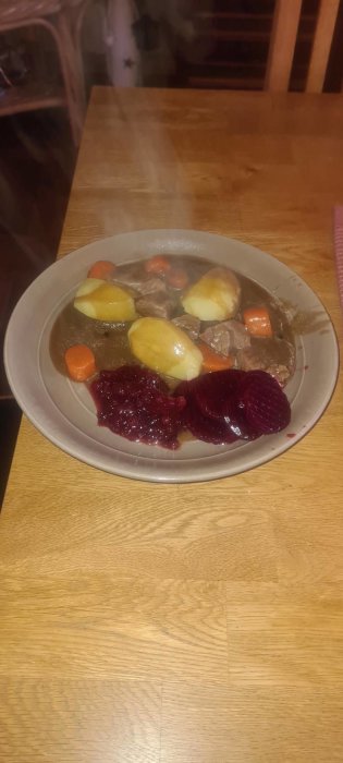 Ett svenskt maträtt, kalops med kokt potatis, morötter, rödbetor och lingonsylt, serverat på ett bord.