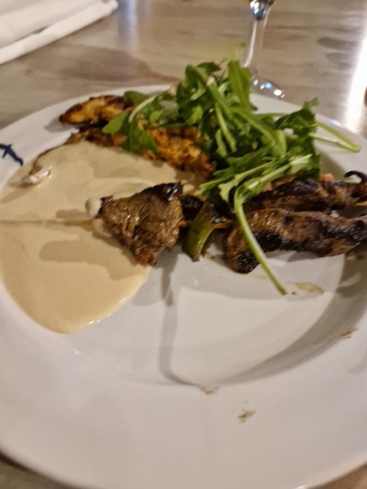 En tallrik med grillad mat, sås och rucola, en gaffel i bakgrunden, suddig förgrund.