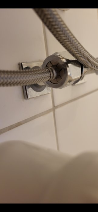 Flexibel duskslang ansluten till vägg i badrum med kakelplattor. Tiltad vy, närbild.
