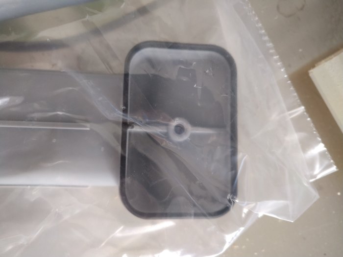 Svart plastföremål i genomskinlig plastpåse, otydliga reflektioner, suddig bakgrund.