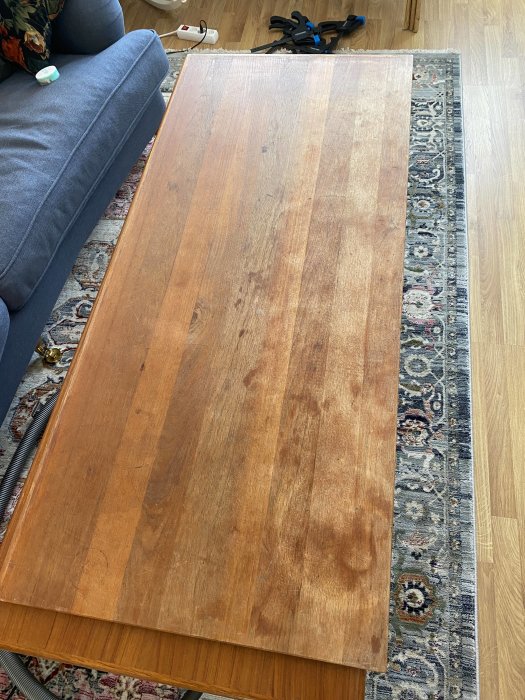 Träbord på orientalisk matta, grå soffa, golv, städsaker i bakgrunden.