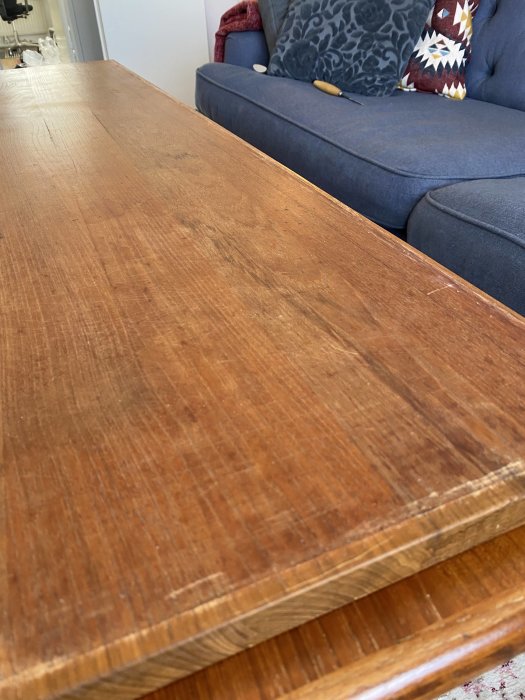 Träbord framför en blå soffa med kuddar, inomhusmiljö, närbild, slitet, detaljrik yta.