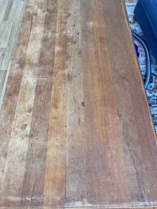 Trägolv med slitage och repor bredvid en soffa med en slang.