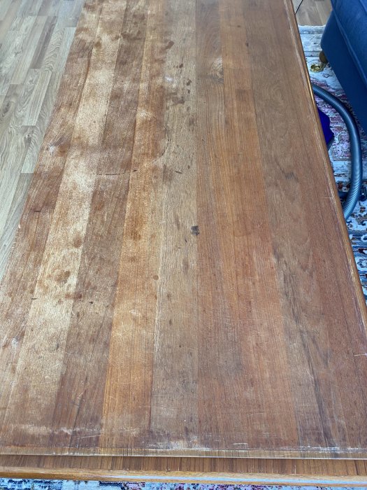 Gammalt slitet träbord med repor och fläckar inomhus, behöver vård eller renovering.