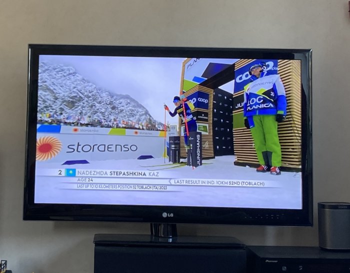 En TV visar skidtävling med idrottare, sponsorer, snöklädda berg och grafik med resultat och information.