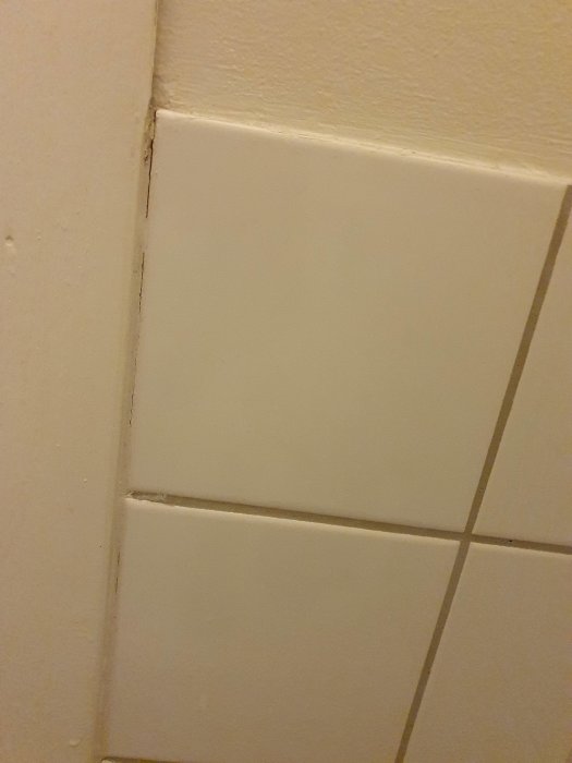 Vit kakelvägg som möter en gipsvägg, synliga fogar och en liten spricka.