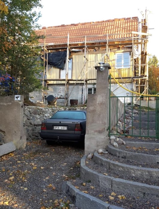 Renovering pågår på ett gult hus med tegeltak, ställning uppställd, bil parkerad framför, höstlöv på marken.