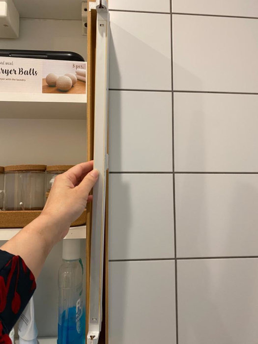 En hand öppnar ett vitt köksskåp; flaskor och förpackning syns inuti.