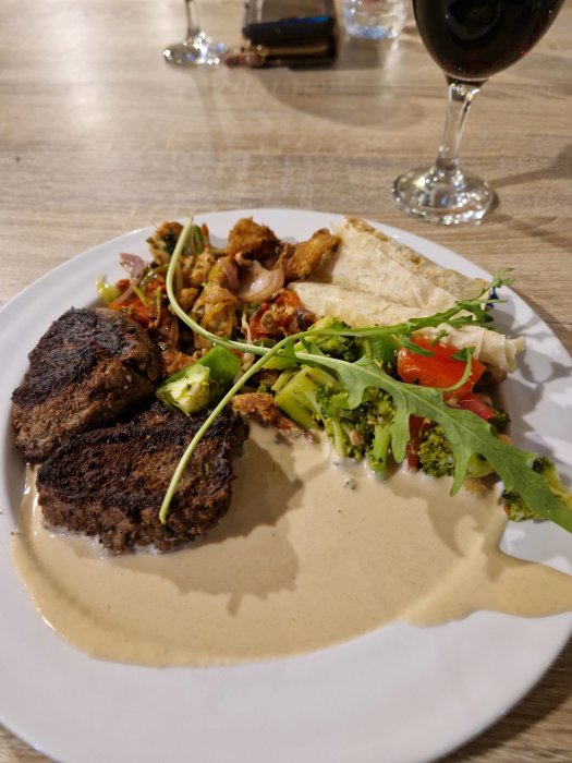 Middagstallrik med biffar, grönsaker, sås och ett glas rödvin. Elegant presentation, matfotografering.