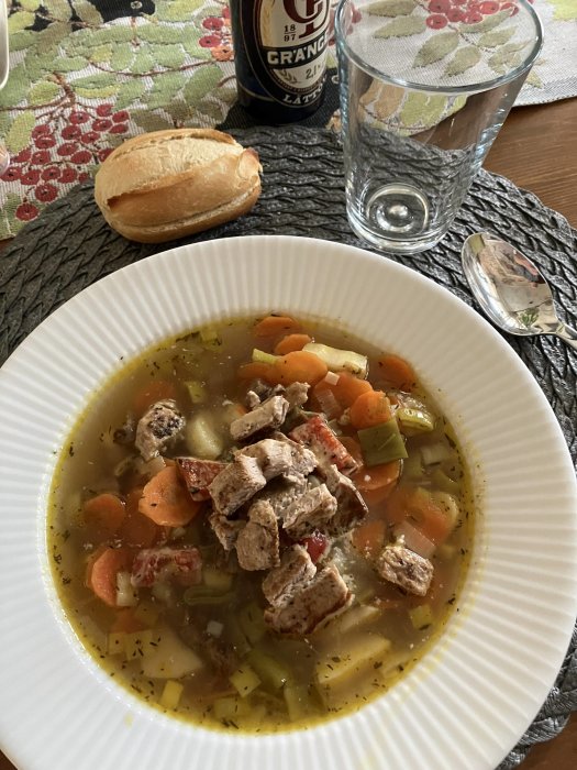 Ett bord med koppargryta, bröd, glas vatten, kött och grönsakssoppa.