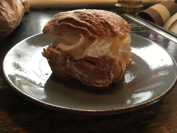 Semla på mörkgrå tallrik, fluffig grädde, skivat vitt bröd, mjöldammade, traditionellt svensk fika.
