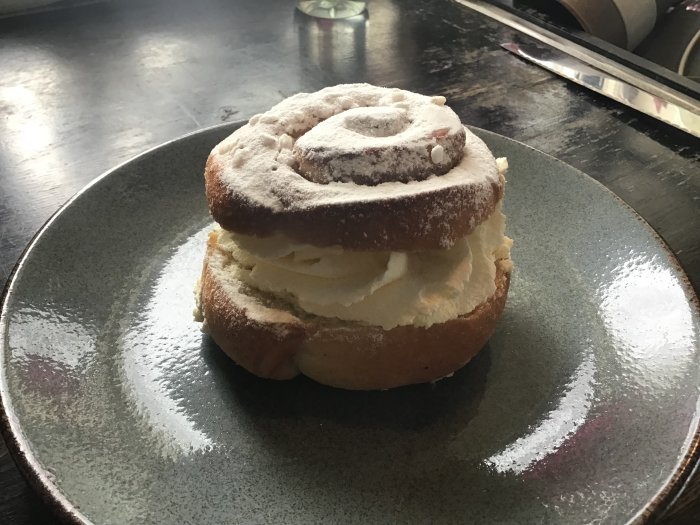 Semla på tallrik, florsocker, grå bakgrund, fettisdagen, gräddbulle, mandelmassa, svenskt traditionellt bakverk.
