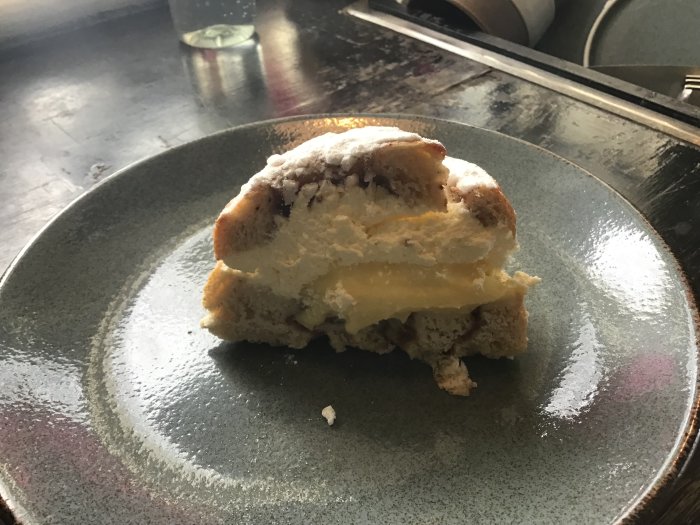 Halväten semla på en keramiktallrik, florsocker strött ovanpå, reflektioner i bakgrunden.
