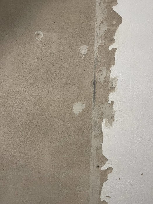 En vägg med delvis skalad avfärgning, visar underliggande rå betong mot vitmålad yta.