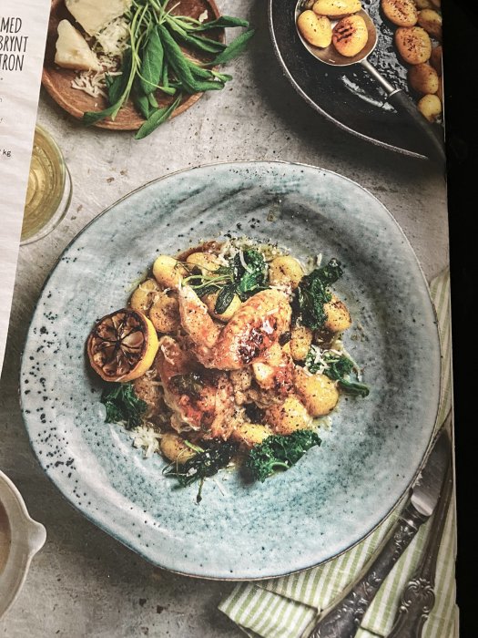 Elegant maträtt med kyckling, gnocchi, grönkål, citron på keramiktallrik, träbricka med örter, glas vin bakgrund.