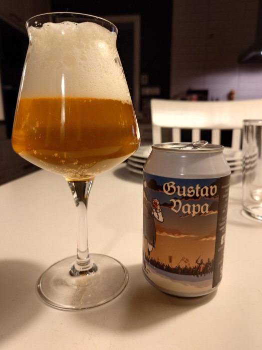 Ett ölglas med skummat öl bredvid en ölburk på ett bord inomhus.
