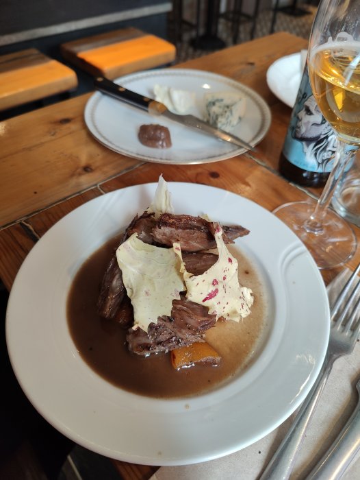 Rätten på bilden ser ut som långkokt kött med sås och purjolök, serverad med ost, choklad och ett glas vin.