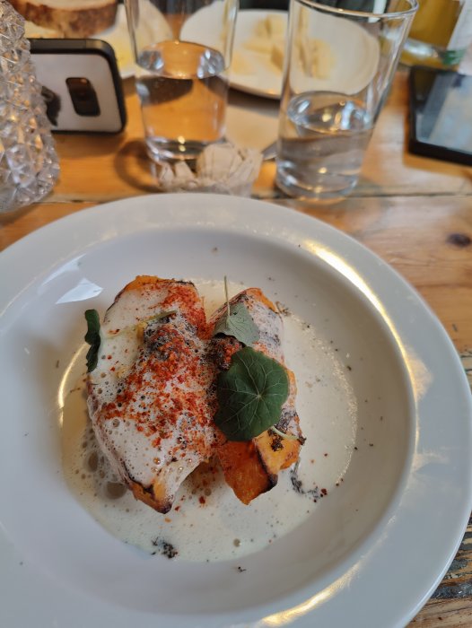 Förrätt på en vit tallrik: grillad fisk, sötpotatis, skum, kryddor, grönt blad, modern presentation, odefinierad restaurangmiljö.