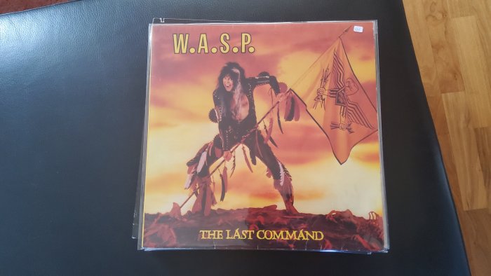 Skivomslag för W.A.S.P.'s "The Last Command", figur i krigarutstyrsel mot solnedgångsbakgrund, flagga hålls i handen.