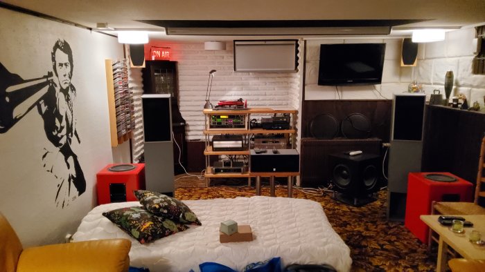 Mysigt källarrum med vintagekänsla, ljudutrustning, soffa, konst, matta, TV och "ON AIR"-ljusskylt.