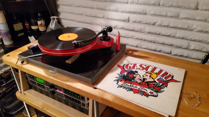 Vinylspelare, skivomslag, ljudutrustning, tegelvägg, flaskor i bakgrunden. Vintage, musik, interiör, hobby.