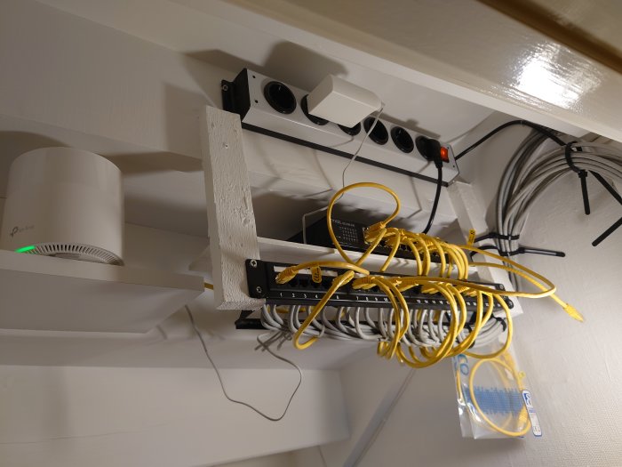 Nätverksutrustning monterad på vägg, inklusive router, switch och Ethernet-kablar, ordnat för internetanslutning.