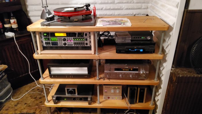 Hyllor med audio-utrustning: förstärkare, equalizer, skivspelare, CD-spelare och kablar. Bakgrund av vit tegelvägg.