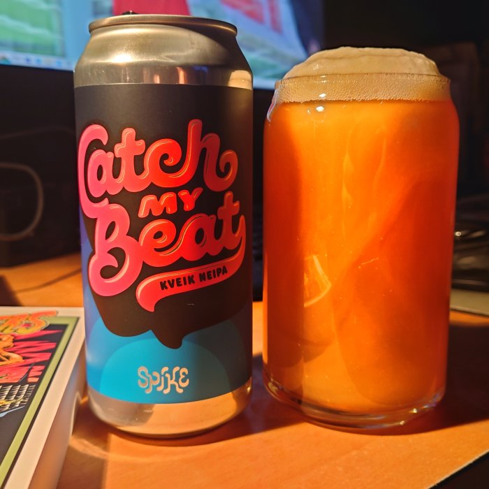 Ölburk med texten "Catch my Beat Kveik NEIPA" bredvid ett fullt glas öl.