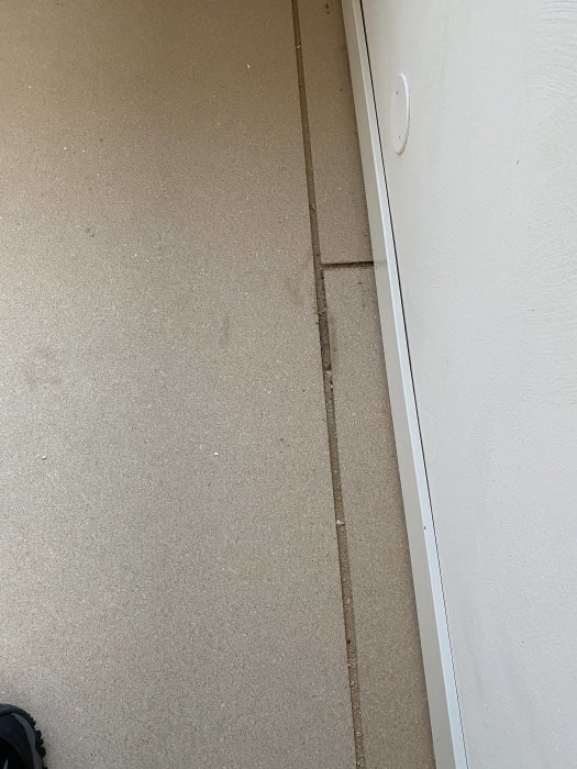 Beige matta, vit vägg och dörrstoppare, mörk kant längs golvet.