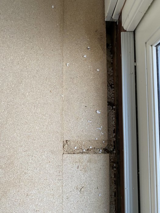 En vägg intill ett fönster med smuts och spruckna rester på golvbeläggningen, tecken på slitage eller skada.