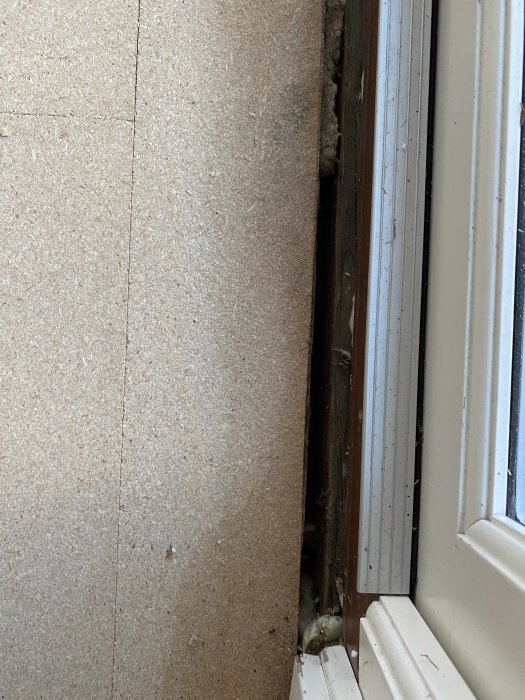 Fönsterram nära en vägg med isolering synlig i glipan; skadad väggstruktur; behov av reparation.
