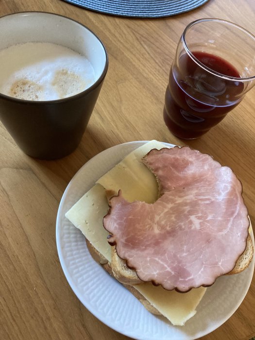 En smörgås med ost och skinka, en kopp kaffe och ett glas juice.