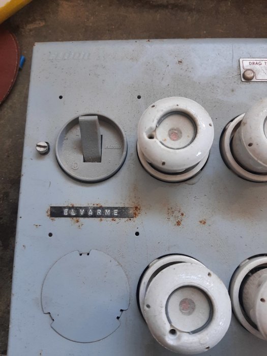 Gammal elektrisk spispanel med vred och knappar, smutsig, sliten, etikett markerad "ELVÄRME".