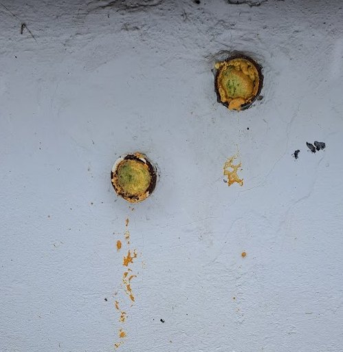 Två runda, rostiga föremål på en smutsvit vägg med fallande orange färgspår.