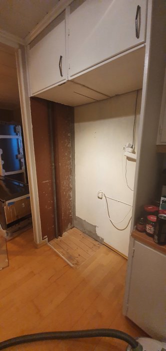 Renovering pågår, väggen partsvis rivet, synliga elinstallationer, ofärdigt parkettgolv, vit skåpinredning, spackel.