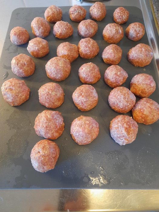 Råa köttbullar ordnade på en bakplåt redo att grillas eller stekas.