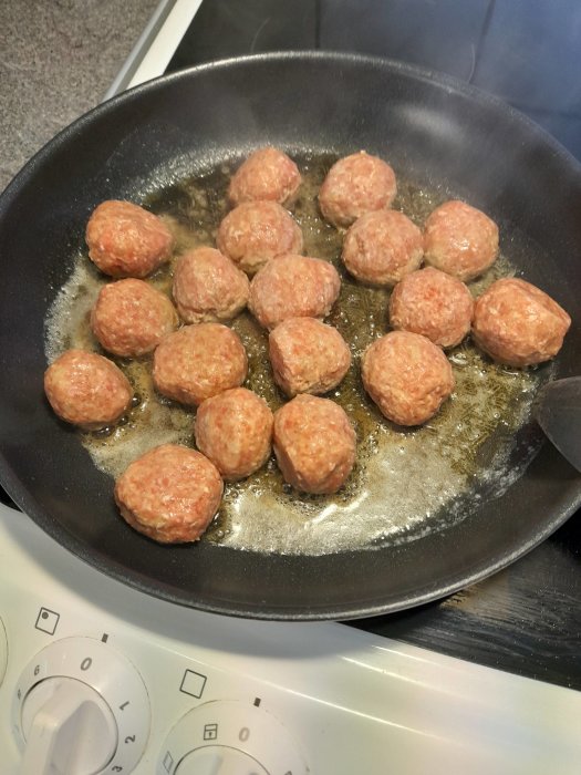 Köttbullar steks i panna på spis, köttbullarna är okokta och spisen är elektrisk. Cooking meatballs in a frying pan.