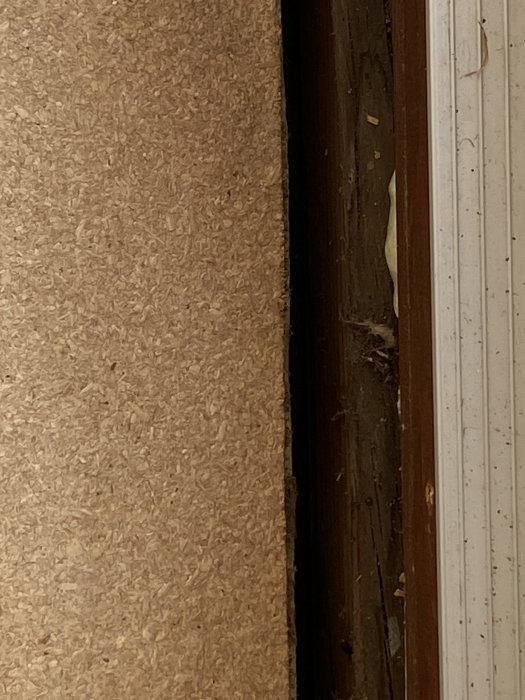 En närbild på en korktavla bredvid en träkant och en dörrpost i förgrunden. Otydlig omgivning, slitet utseende.