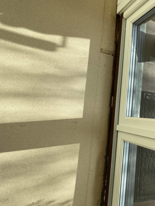 Soligt fönsterprojicerat skuggmönster på en beigefärgad vägg och golv, tydliga ljus och skuggspel.